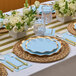 A Sophistiplate Sky Blue paper guest towel with a spoon and fork on a blue napkin on a table with blue plates and gold place settings.