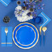 A blue table setting with Sophistiplate blue cocktail napkins, a blue and gold plate, and a blue glass with a blue stripe.