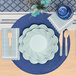 A Sophistiplate sky blue scalloped edge paper guest towel on a table with a blue and white place setting.