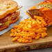 A sandwich with bacon and cheese on a cutting board with a bag of Cheetos cheese snacks.