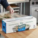 A person wearing gloves uses Choice Safecut premium foodservice film to cover a tray of food.