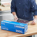 A person in gloves uses Choice Heavy-Duty Foodservice Film to cover a blue container of food.