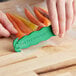 A hand using a green Klever Kutter box cutter to open a bag of carrots.