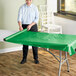 A person rolling a green plastic table cover onto a table.