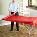 A woman rolling a red Choice tablecloth on a table.