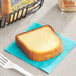 An individually wrapped Ne-Mo's Bakery all butter pound cake slice on a blue napkin next to a fork and a container of butter.