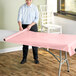 A woman rolling a Choice pink plastic table cover on a table.