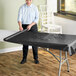 A woman rolling a Choice black plastic table cover onto a table.