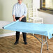 A person rolling a light blue plastic table cover on a table.