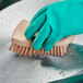 A gloved hand using a Carlisle Sparta tan handheld scrub brush to clean a stainless steel pan.