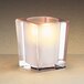 A Sterno frosted clear glass square candle holder with a lit candle inside.