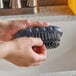 A person holding a Carlisle Sparta black hand and nail brush over a sink.