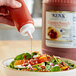 A hand pouring Ken's Country French dressing onto a bowl of salad.