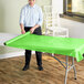 A woman rolling a lime green plastic table cover onto a table.