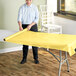 A woman rolling a Choice yellow plastic table cover on a table.