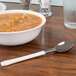 A bowl of soup and a WNA Comet Reflections Duet ivory plastic teaspoon on a table.