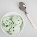 A bowl of mint chocolate chip ice cream with a WNA Comet Reflections Duet ivory plastic teaspoon.