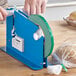 A blue tape dispenser with a Lavex green tape roll being used to seal a bag of bread
