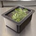 A Cambro black food pan filled with green leaves on a counter in a salad bar.