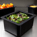 A Cambro black 1/2 size food pan on a counter with salad inside.