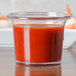 A Carlisle clear round plastic sauce cup filled with red liquid.
