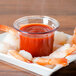 A plate of shrimp with Carlisle clear plastic sauce cups filled with red sauce.