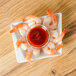 A white plate with a shrimp and a Carlisle clear plastic sauce cup filled with red sauce on it.