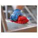 A gloved hand using a Vikan red scrub brush to clean a metal surface.