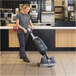 A woman using a NaceCare compact floor scrubber to clean a floor in a commercial space.