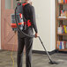 A man wearing a grey and red NaceCare backpack vacuum cleaner vacuuming the floor.
