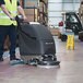 A man using a NaceCare Solutions cordless walk behind floor scrubber with a black cover to clean a warehouse floor.