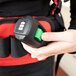 A person using a green button to operate a NaceCare Solutions corded backpack vacuum.