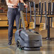 A woman using a NaceCare walk behind floor scrubber to clean a floor.