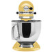 A KitchenAid Artisan Series Majestic Yellow 5-quart stand mixer on a counter with a silver bowl.