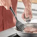 A person using a Choice black slotted turner to cook meat in a pan.