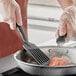 A person cooking salmon in a pan with a Choice black slotted fish turner.