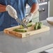 A person cutting cucumbers on a Choice wood cutting board.