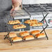 A woman using a Wilton 3-tier cooling rack to display pastries.