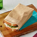 A sandwich in a Bagcraft natural paper wrap bag on a cutting board.