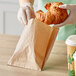 A person in gloves holding a croissant in a Bagcraft EcoCraft brown paper bag.