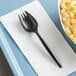 A black Remcoda plastic spork on a white napkin next to a bowl of macaroni and cheese.