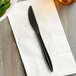 A Remcoda black plastic knife on a white napkin next to a plate.