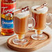 Two glass mugs of brown liquid with Torani Cinnamon Flavoring Syrup and cinnamon sticks.