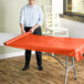 A woman rolling a red Table Mate plastic table cover onto a table outdoors.