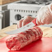 A person using a Victorinox Breaking Knife to cut meat on a cutting board.