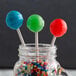 A jar with blue lollipops on paper sticks on a counter.
