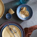 A table setting with Libbey blue terracotta bowls, plates, and cutlery on an outdoor patio.