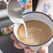 A person pouring Almond Breeze Barista Collection Unsweetened Almond Milk into a cup of coffee.