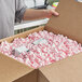 A person holding a white box full of Lavex pink anti-static packing peanuts.