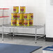 A metal shelf with a group of cans, including a yellow can of beans, on it.
